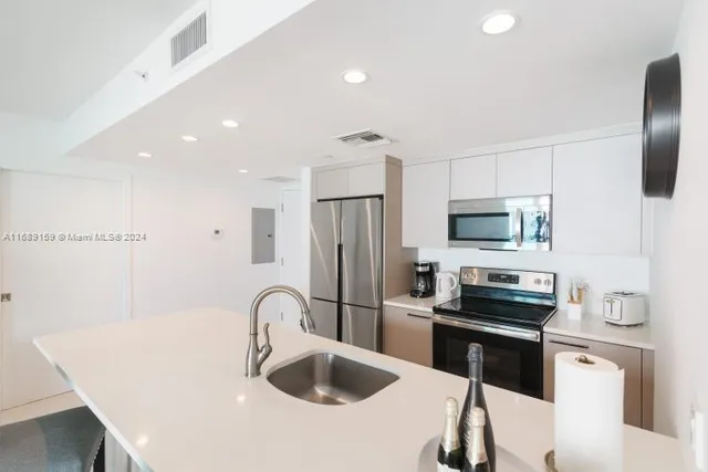 a kitchen with stainless steel appliances kitchen island a refrigerator sink and white cabinets