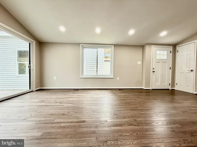 an empty room with wooden floor and windows with curtains