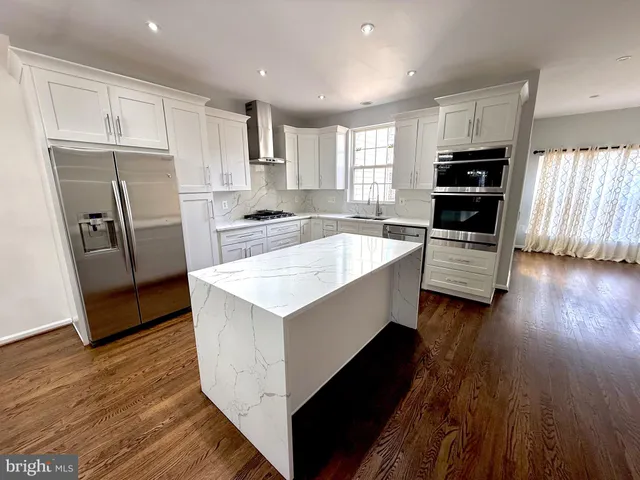 a large kitchen with stainless steel appliances kitchen island granite countertop a stove a refrigerator a sink and dishwasher with wooden floor