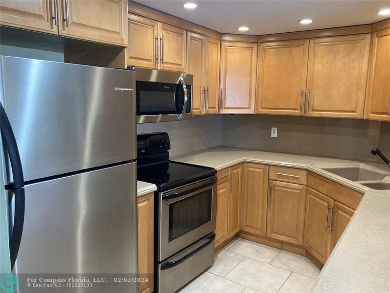 a kitchen with stainless steel appliances granite countertop a refrigerator a stove and a sink with wooden cabinets