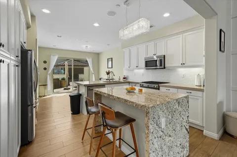 a kitchen with stainless steel appliances granite countertop a refrigerator a stove top oven a sink dishwasher and white cabinets with wooden floor