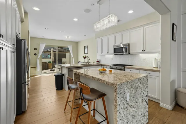 a kitchen with stainless steel appliances granite countertop a refrigerator a stove top oven a sink dishwasher and white cabinets with wooden floor