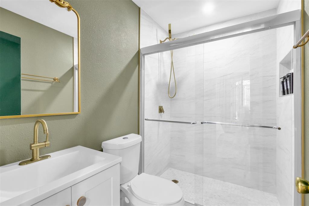 4121 Junius Street, Unit B Dallas, TX 75246 - Photo 16 of 32 Bathroom featuring a frameless glass shower enclosure, white subway tile shower surround, shower niche, white vanity with integrated sink, and brass-finish fixtures