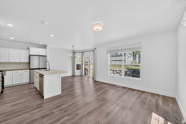 14771 Haddington Road Draper, UT 84020 - Photo 7 of 44 Open-concept living area featuring wood-finish flooring, a kitchen island with sink and integrated dishwasher, white cabinetry with stainless steel appliances, and a dining area with a chandelier
