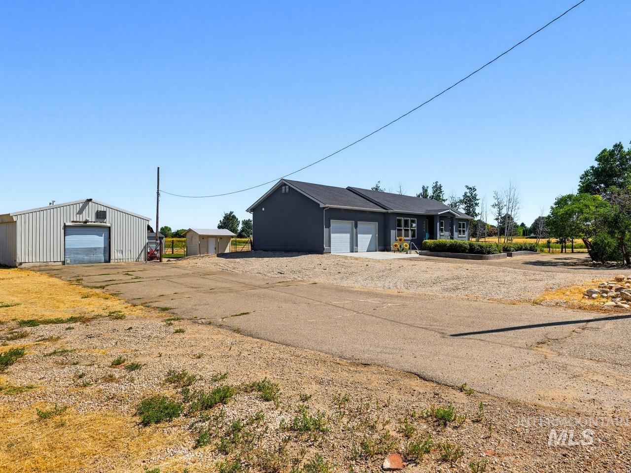 4950 West Columbia Road Nampa, ID 83687 - Photo 49 of 50 Property featuring a detached metal-sided outbuilding with roll-up door, a separate small utility building, and a main residence with a two-car garage and dark gray exterior siding