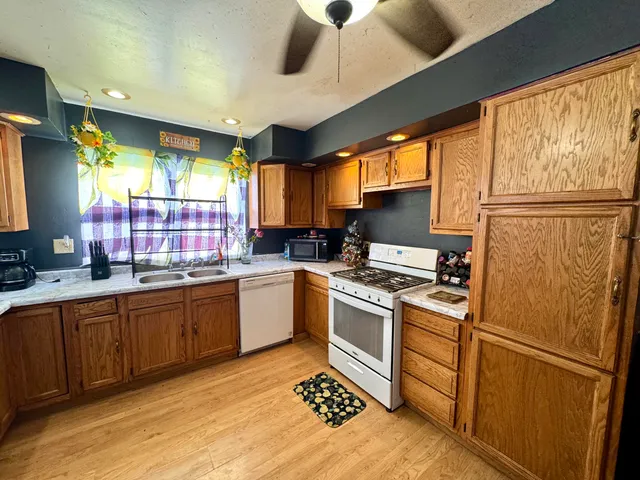 a kitchen with stainless steel appliances granite countertop a refrigerator a sink dishwasher a stove and white countertops with wooden floor