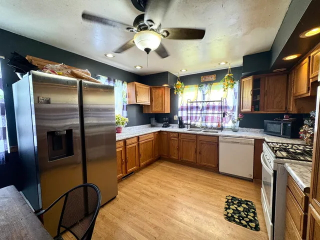 a kitchen with stainless steel appliances kitchen island granite countertop a refrigerator a sink dishwasher a stove and a dining table with wooden floor