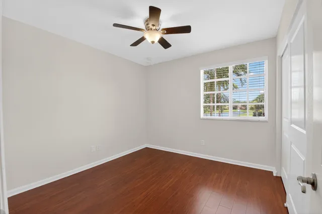 an empty room with wooden floor ceiling fan and windows