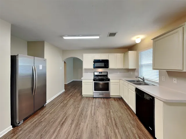 a kitchen with stainless steel appliances granite countertop a refrigerator a stove top oven a sink dishwasher and wooden floor