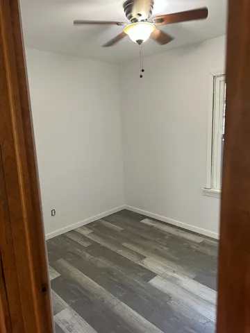 an empty room with a chandelier fan and wooden floor