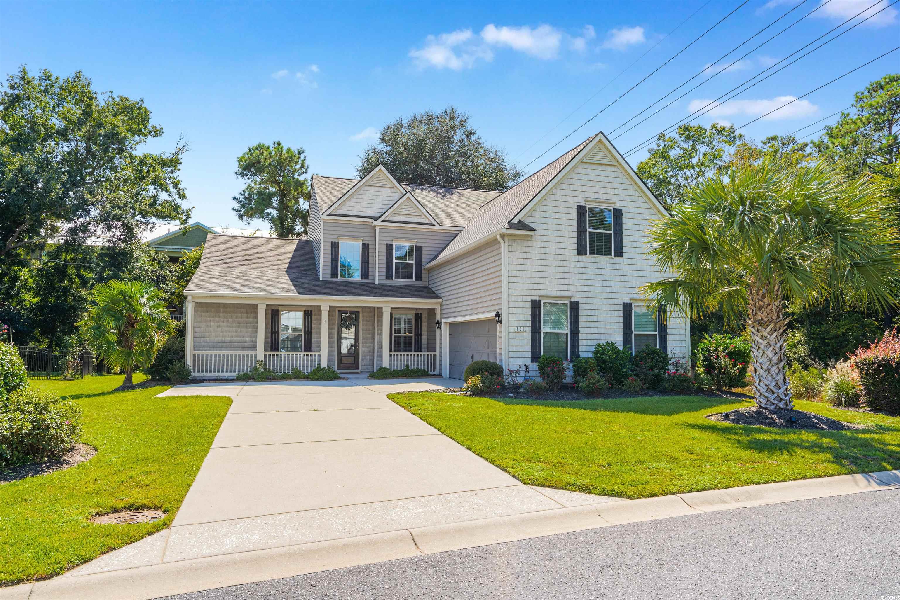 View of front of house with a porch, a front lawn, driveway, a garage, and roof with shingles