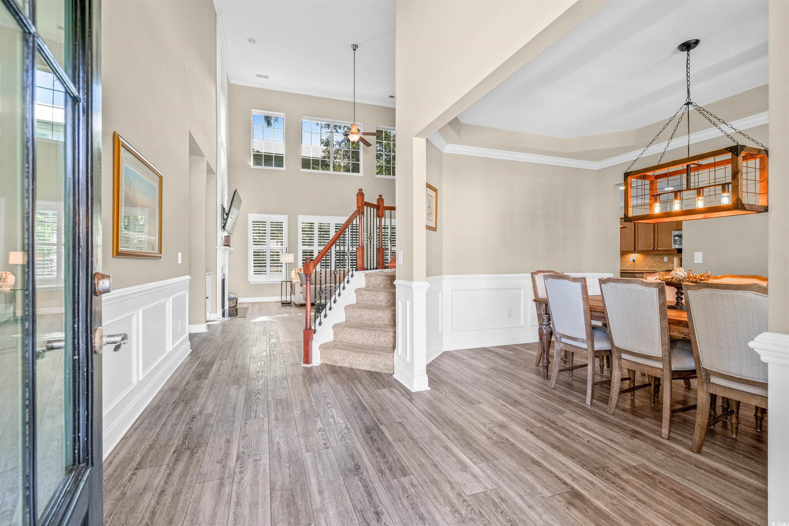 Entryway featuring light wood finished floors, stairway, a tray ceiling, crown molding, and wainscoting