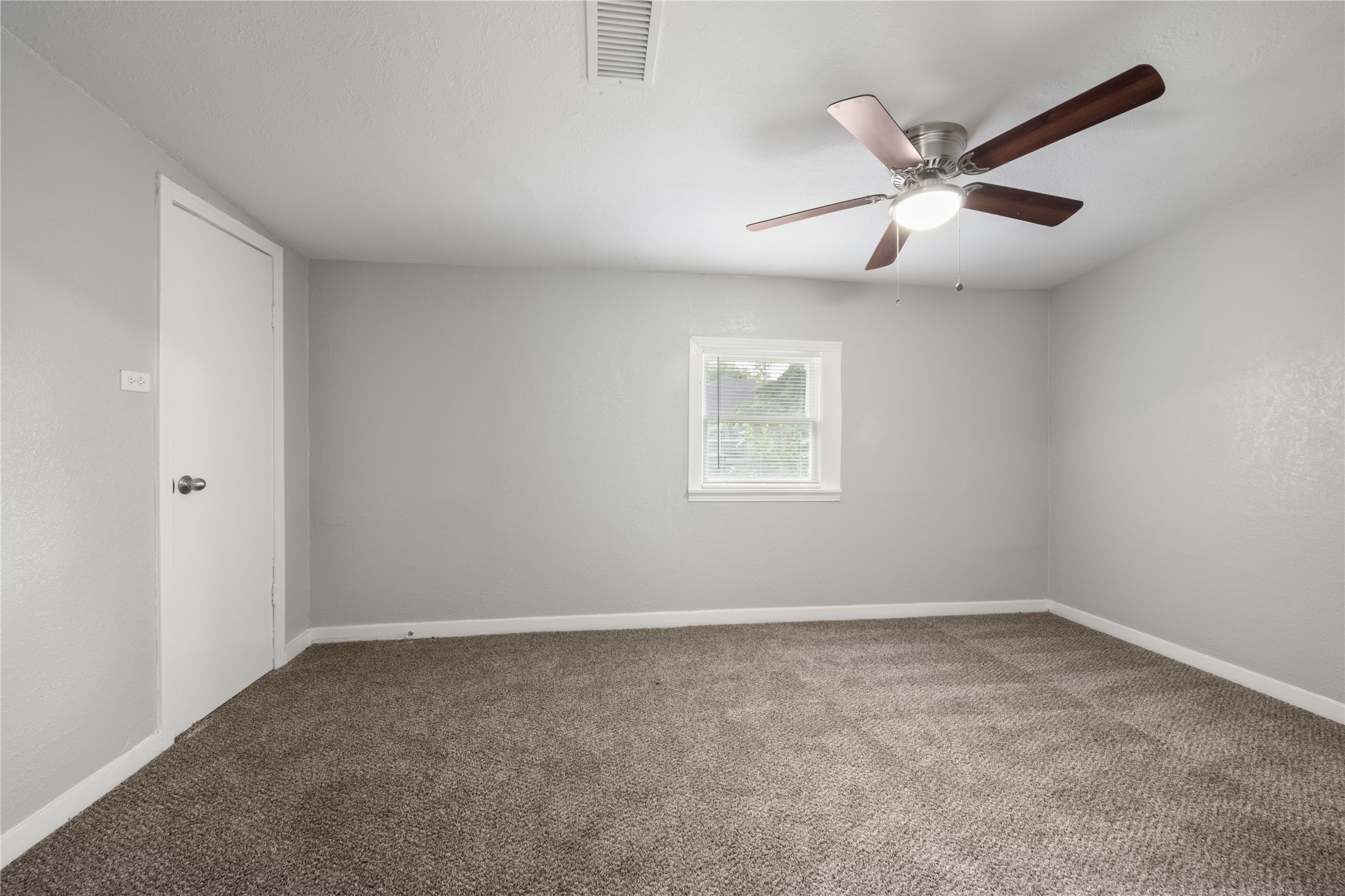 9210 Compton Street Houston, TX 77016 - Photo 21 of 50 Spacious bedroom with neutral tones features plush carpeting, a ceiling fan, and ample natural light from a central window.