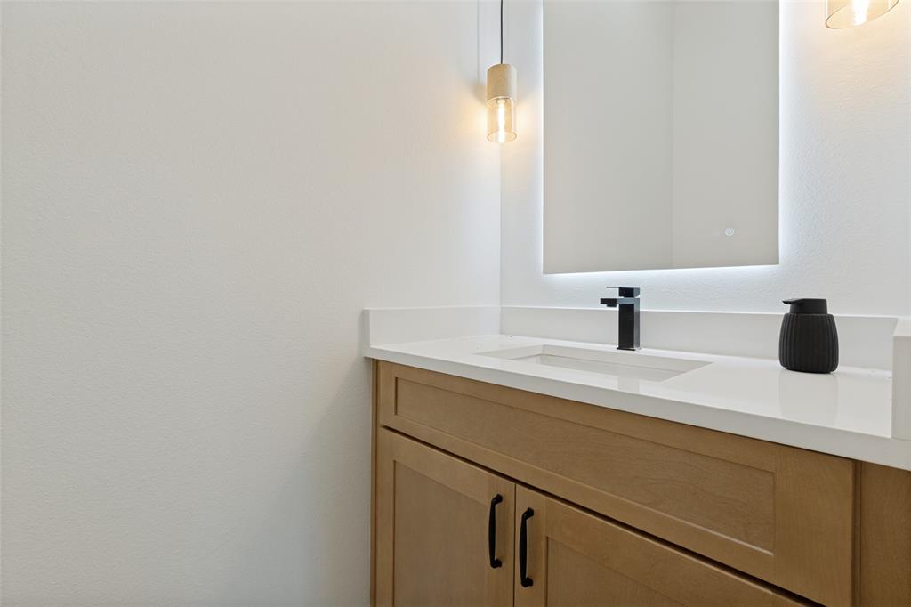 1143 Riverwood Road Dallas, TX 75217 - Photo 18 of 24 Modern vanity featuring a light wood-finish cabinet with matte black hardware, a pristine white countertop, and an undermount sink