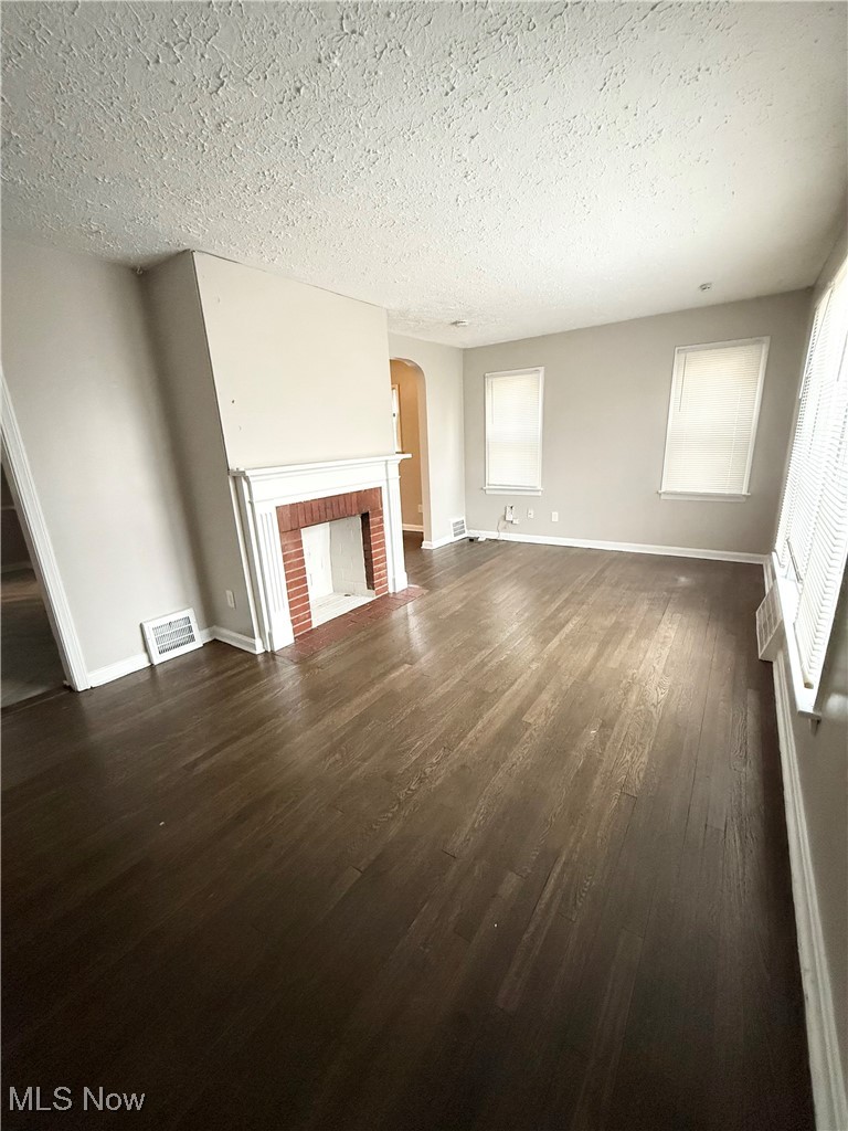 Unfurnished living room featuring a fireplace, arched walkways, dark wood finished floors, and a textured ceiling