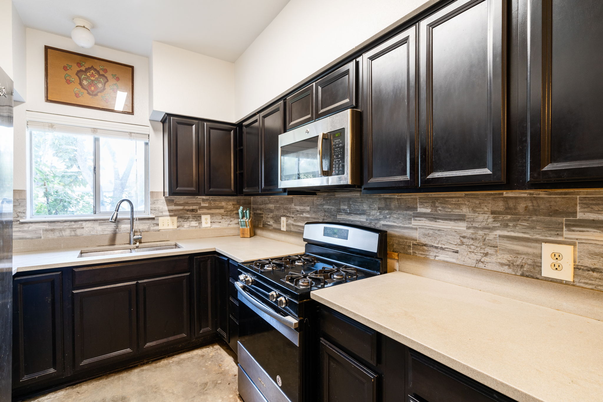 5611 Meadow Crest Austin, TX 78744 - Photo 8 of 26 Kitchen with stainless steel appliances, dark wood finish cabinets, tasteful backsplash, and light stone countertops