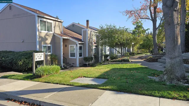 a view of a white house next to a yard with big trees and plants