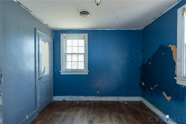 an empty room with wooden floor and windows with curtains