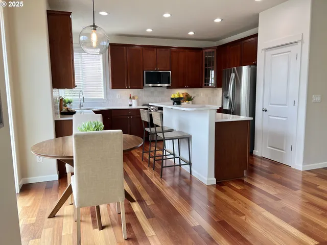 a kitchen with stainless steel appliances kitchen island granite countertop a refrigerator a stove top oven and a dining table with wooden floor