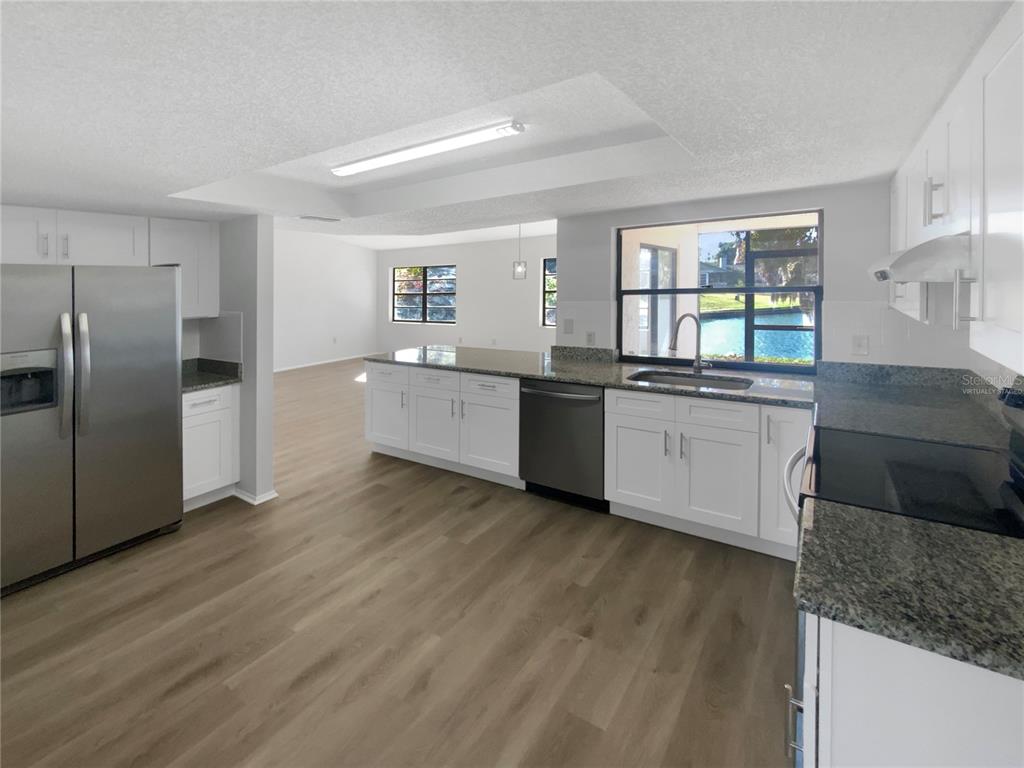 7846 Cayuga Drive New Port Richey, FL 34653 - Photo 2 of 32 a kitchen with stainless steel appliances granite countertop a sink and dishwasher a refrigerator with wooden floors