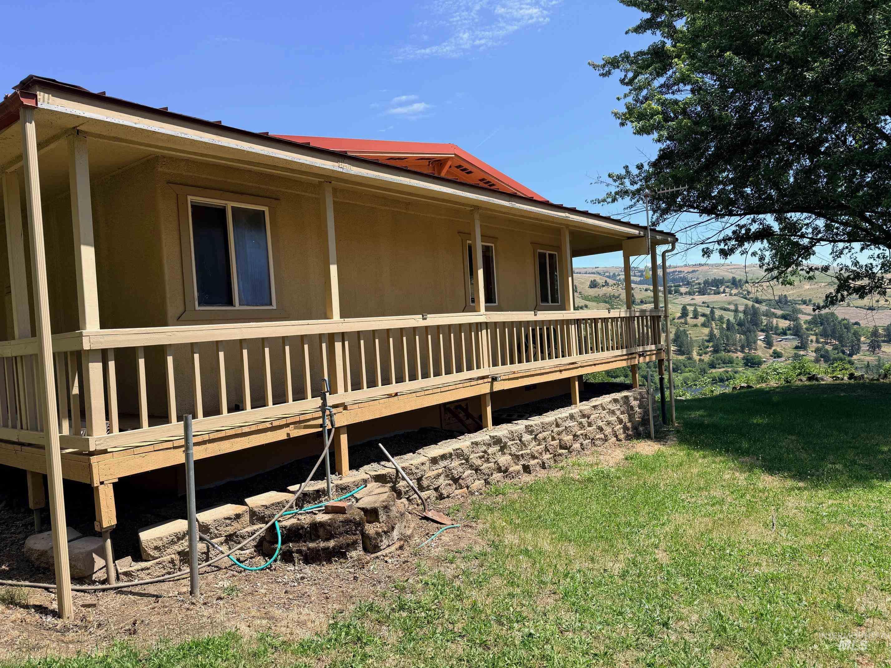 35322 River Road Lenore, ID 83541 - Photo 36 of 42 Exterior showcasing a wrap-around porch with wooden railing, stucco siding, and a red metal roof