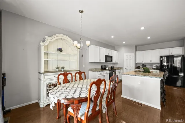 a dinning area with stainless steel appliances kitchen island granite countertop a dining table chairs and a white cabinet