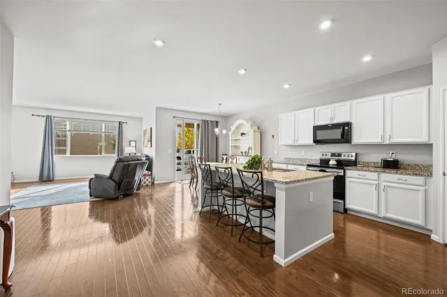 a kitchen with granite countertop a refrigerator a stove a dining table and chairs with wooden floor