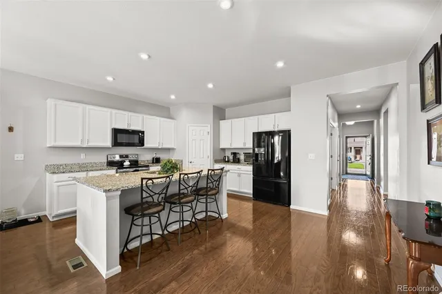 a kitchen with stainless steel appliances a refrigerator a stove top oven a sink a dining table and chairs with wooden floor