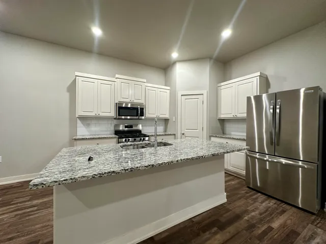 a kitchen with kitchen island granite countertop a refrigerator a stove and a sink