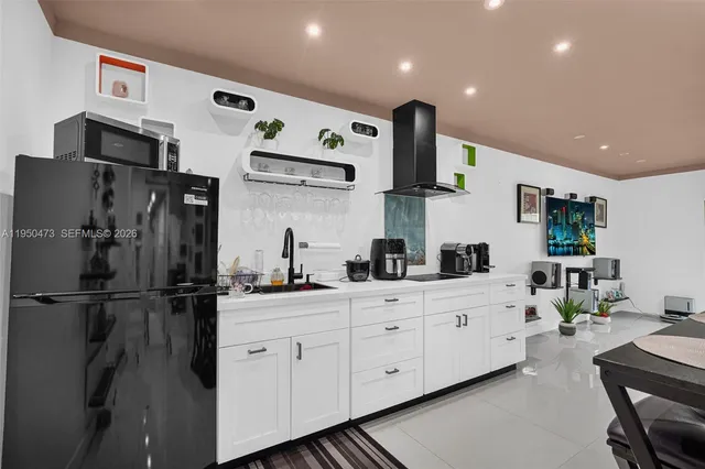 a kitchen with stainless steel appliances kitchen island granite countertop a refrigerator a sink dishwasher and white cabinets with wooden floor