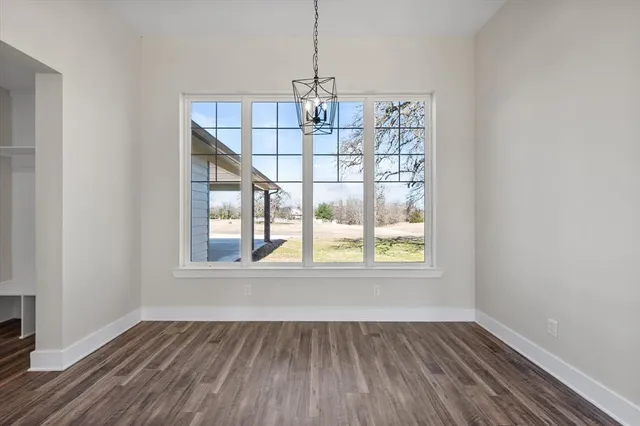 an empty room with wooden floor chandelier and windows