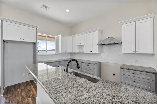 a kitchen with granite countertop a stove a sink and white cabinets