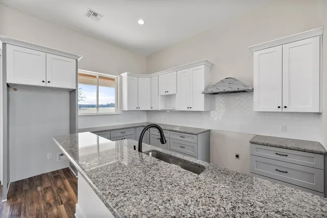 a kitchen with granite countertop a stove a sink and white cabinets