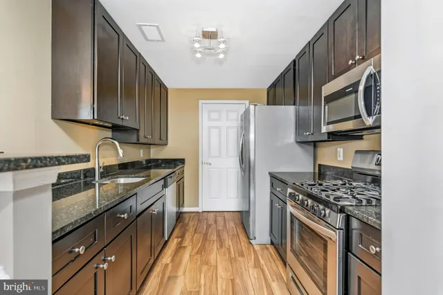 a kitchen with stainless steel appliances granite countertop a stove top oven a sink dishwasher a refrigerator and cabinets with wooden floor