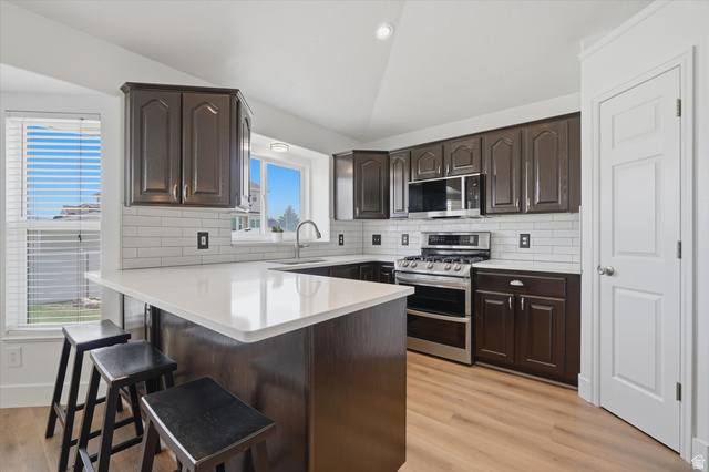 5576 South 4100th Street West Roy, UT 84067 - Photo 7 of 35 Modern kitchen featuring dark wood cabinetry, white subway tile backsplash, LVP flooring, and quartzite
