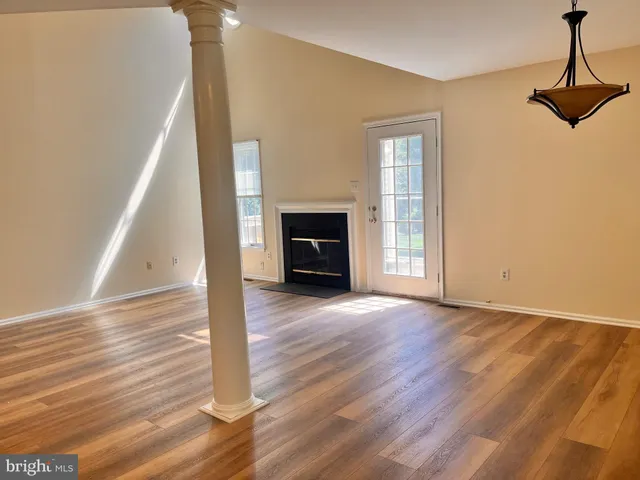 a view of an empty room with wooden floor fireplace and a window