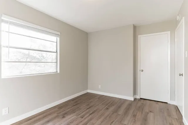 a view of an empty room with wooden floor and a window