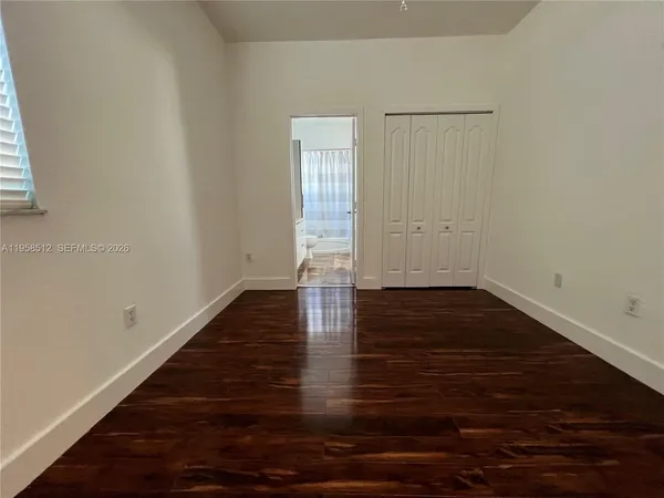 an empty room with wooden floor closet and windows