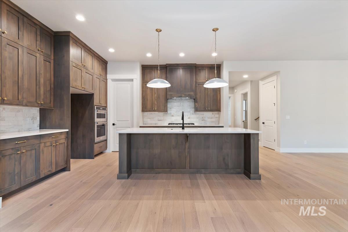 2147 East Blakehurst Avenue Kuna, ID 83634 - Photo 8 of 43 Kitchen with decorative light fixtures, light stone counters, light wood finished floors, decorative backsplash, and dark brown cabinetry