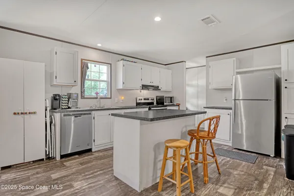a kitchen with stainless steel appliances granite countertop a refrigerator a sink a stove a dining table and chairs