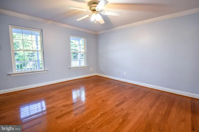 an empty room with wooden floor windows and fan