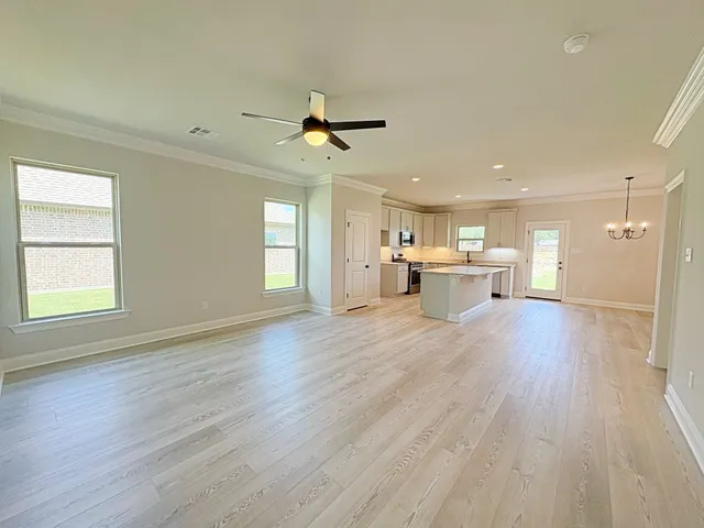 a view of an empty room and a kitchen with a wooden floor