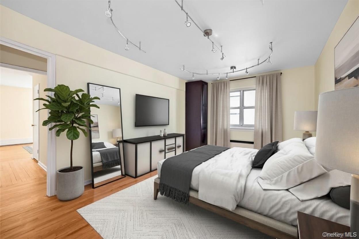 99-10 60th Avenue, Unit 5D Queens, NY 11368 - Photo 4 of 9 a bedroom with a large bed a flat tv screen and potted plant on the dresser