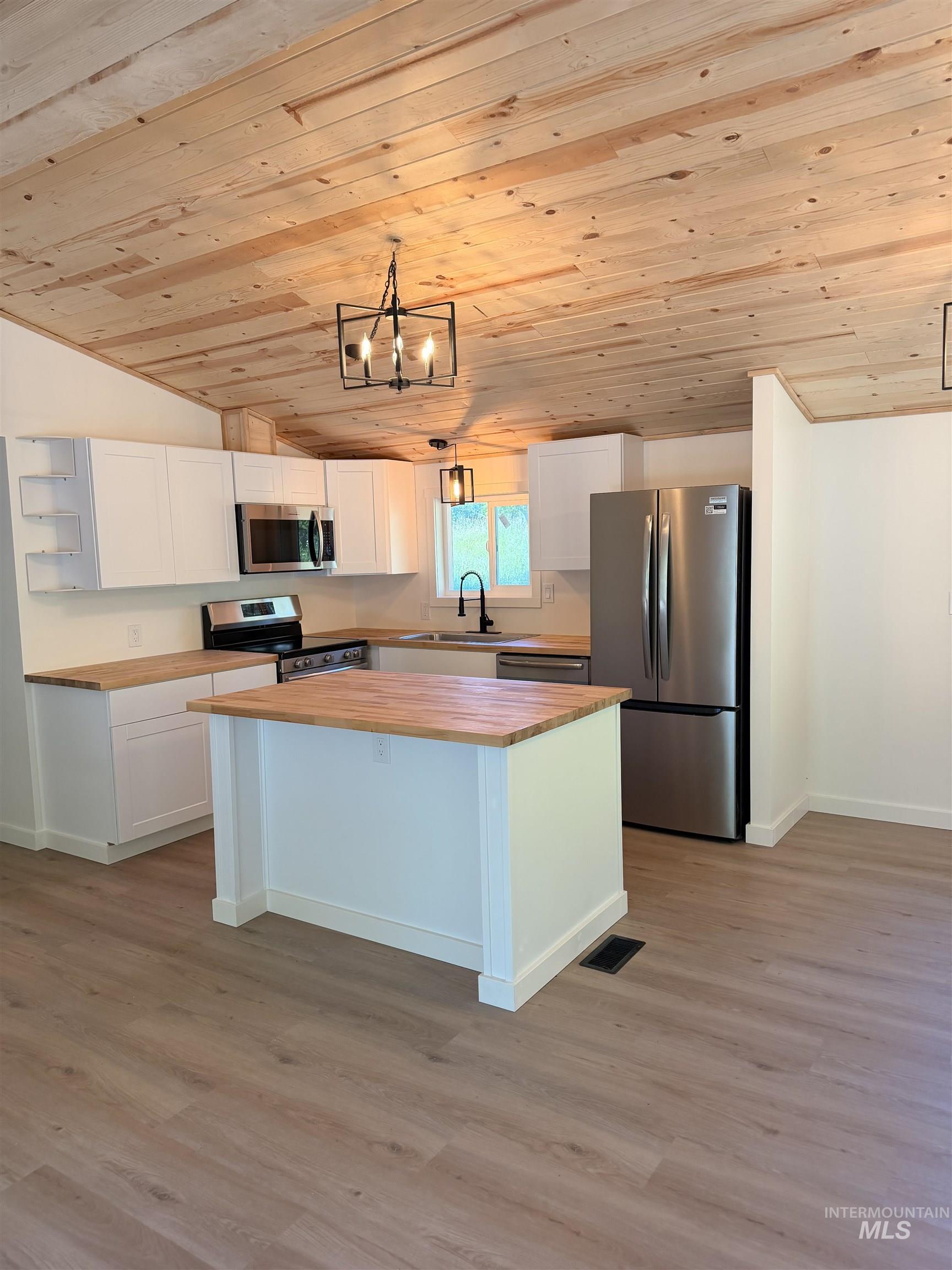 151 View Road Kamiah, ID 83536 - Photo 2 of 49 Modern kitchen featuring a central island, wood-finish countertops, stainless steel appliances, white cabinetry, and wood-paneled vaulted ceilings