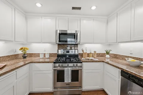 a kitchen with granite countertop white cabinets and stainless steel appliances