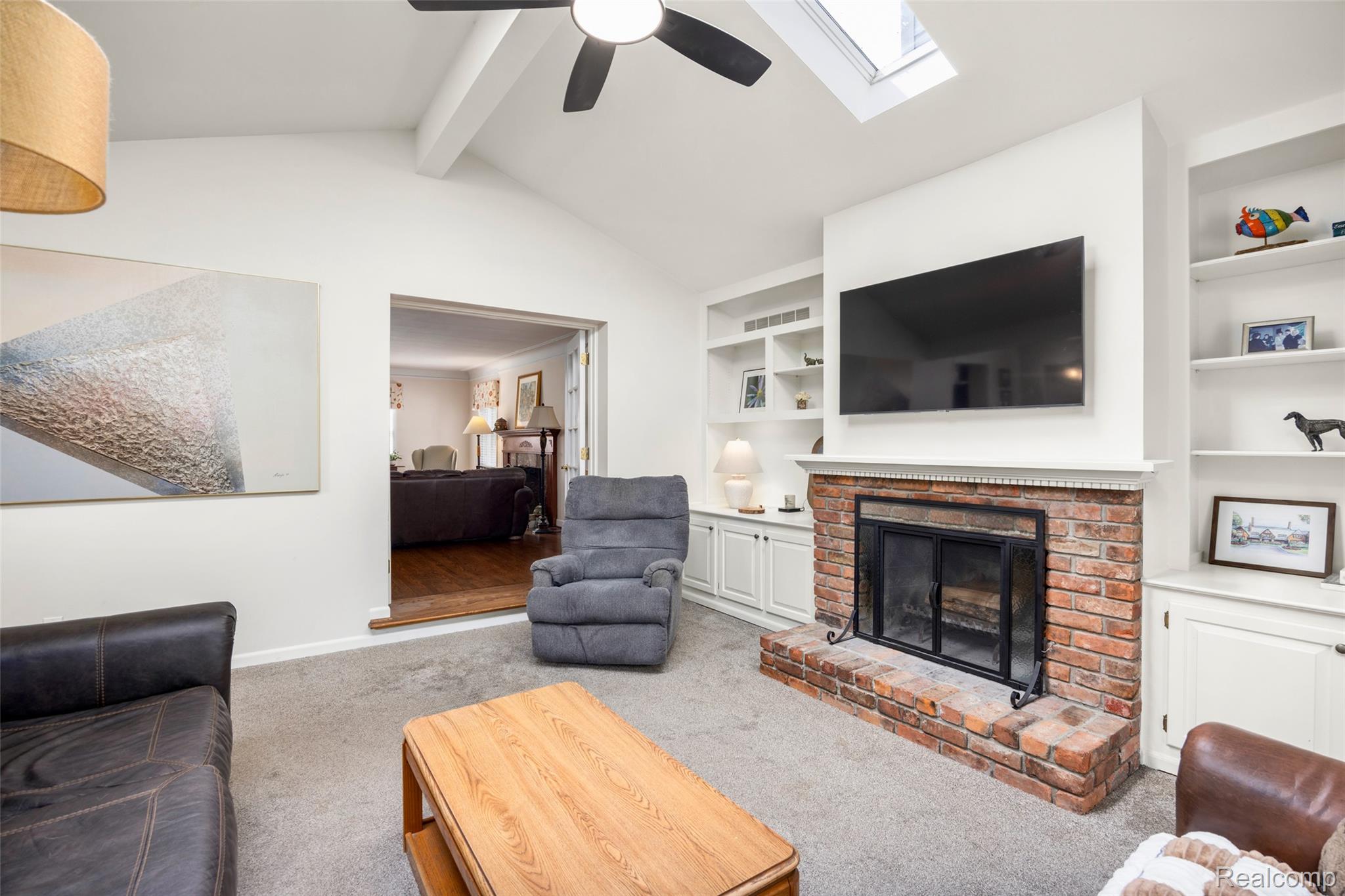 244 Kerby Road Grosse Pointe, MI 48236 - Photo 14 of 53 Living room featuring carpet flooring, lofted ceiling with beams, a ceiling fan, a skylight, and a brick fireplace