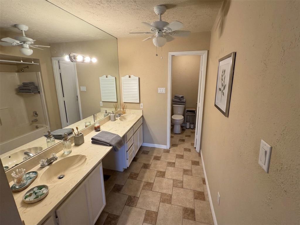 2051 Embassy Way Carrollton, TX 75006 - Photo 14 of 20 Bathroom featuring double vanity, a ceiling fan, a textured ceiling, stone finish flooring, and bathing tub / shower combination