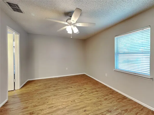 an empty room with wooden floor fan and windows