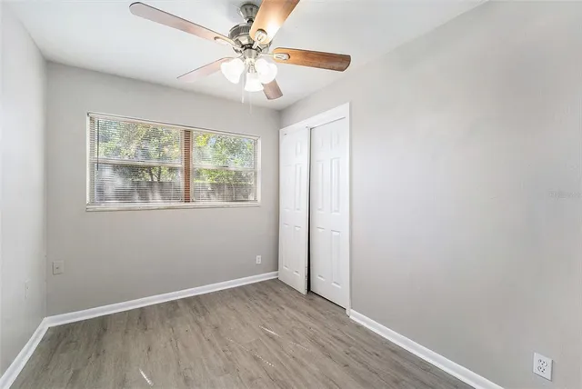 an empty room with wooden floor chandelier fan and windows