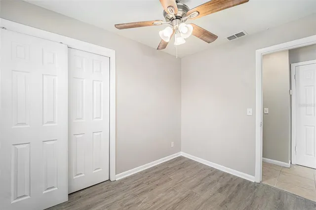 an empty room with wooden floor closet fan and windows